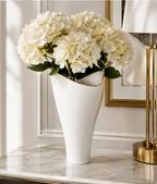Tall white porcelain vase with gold trim filled with white flowers in an elegant interior