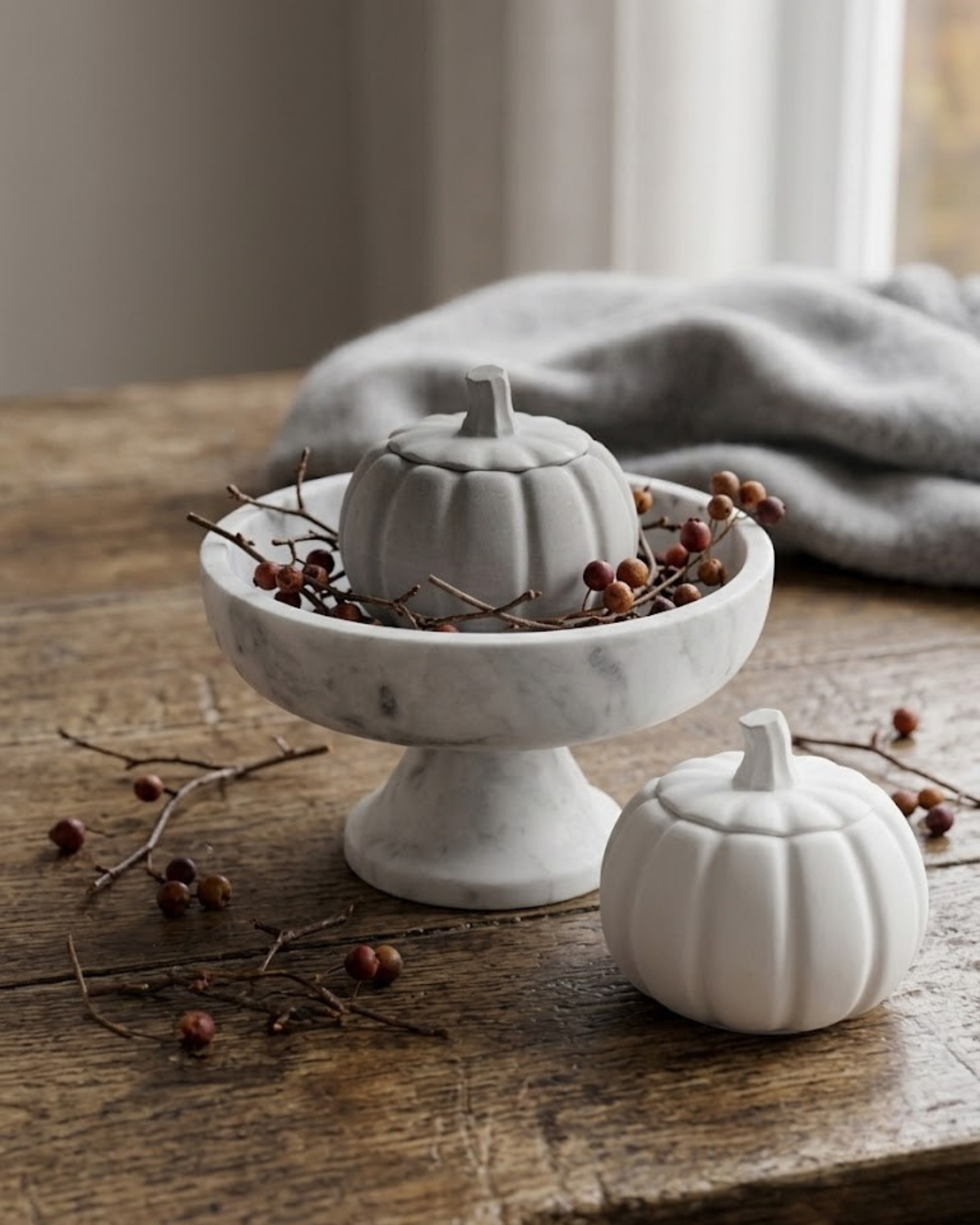     White and gray pumpkin shaped candle jars with lit candles in an elegant neutral autumn displa