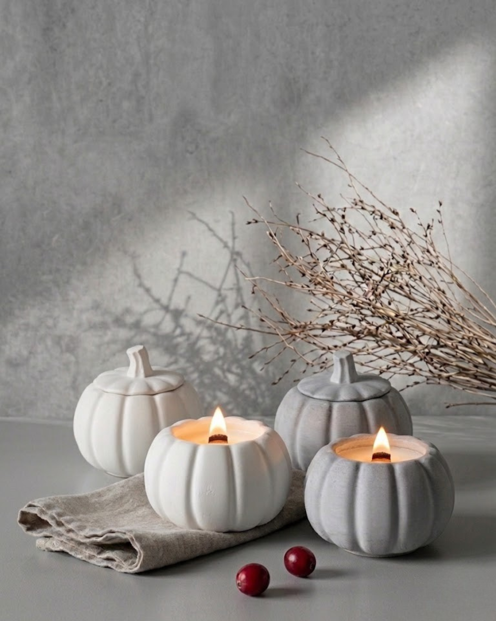 Lit white pumpkin candle jars styled with berries on a rustic table for cozy fall home decor